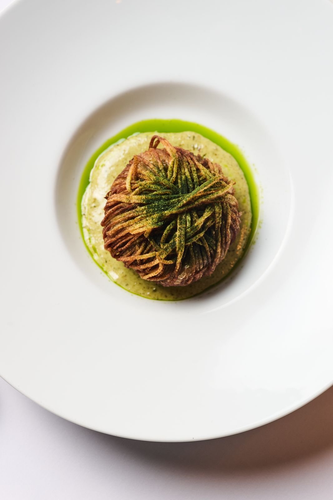 A crisp potato nest on bright green sauce, plated at Delmonico's