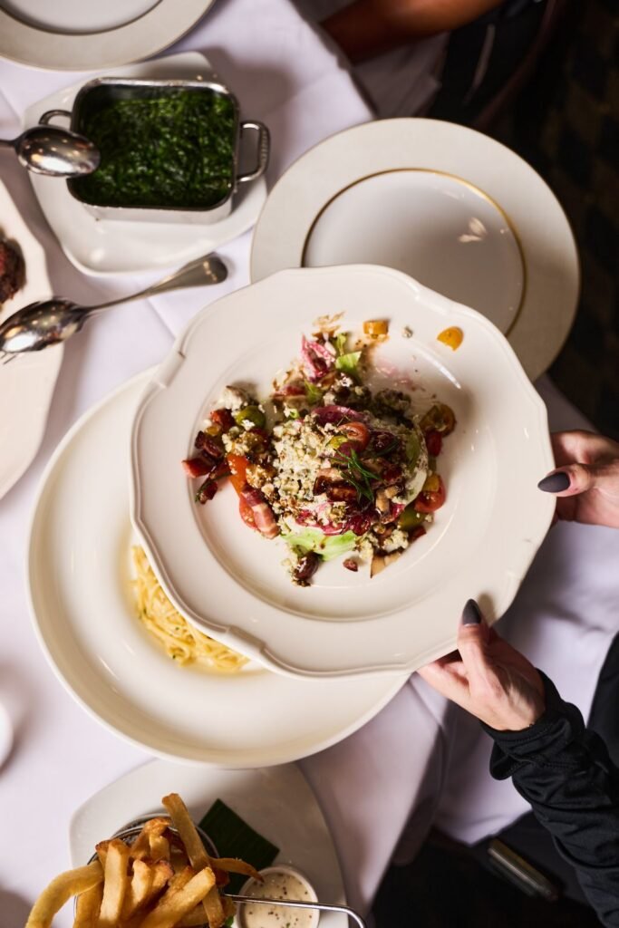 Hands serving steak and sides across a Delmonico's table