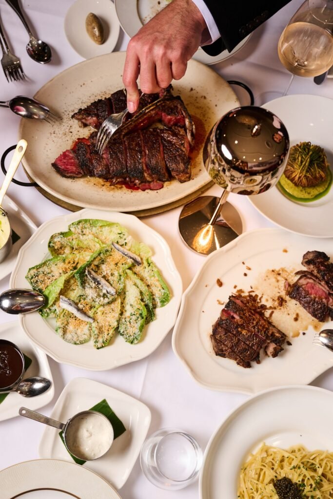 Overhead view of a Delmonico's table as a steak is carved, with sides and wine