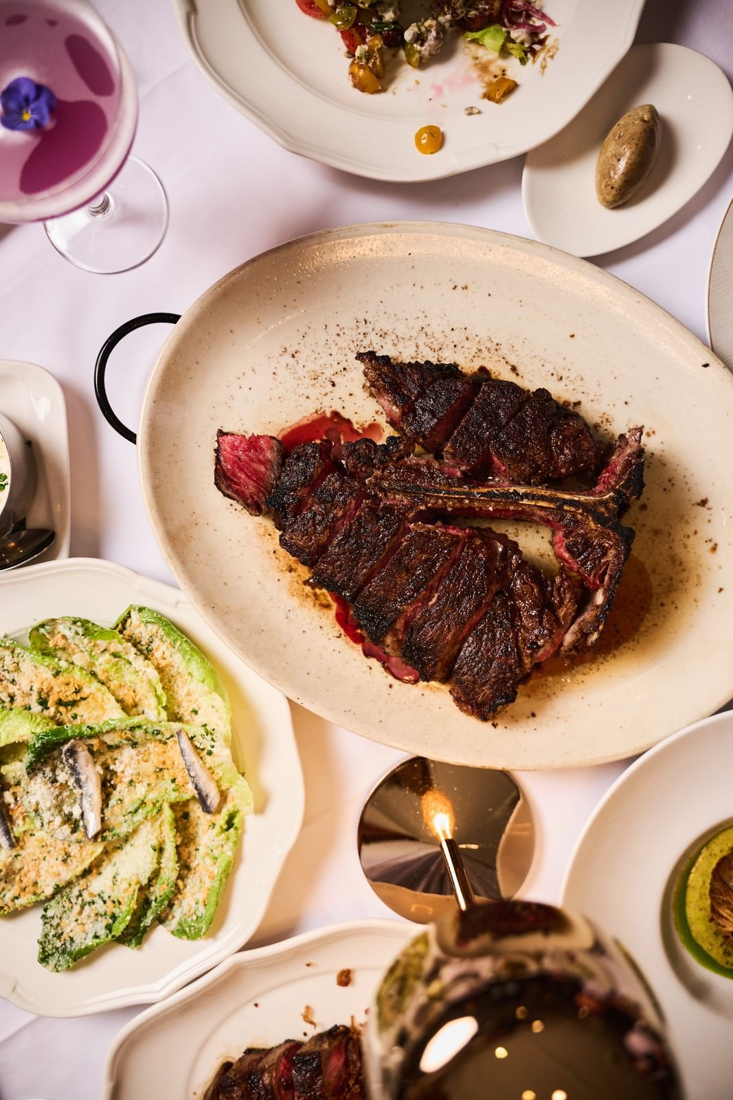 Overhead view of a Delmonico's table with a porterhouse, sides, and wine
