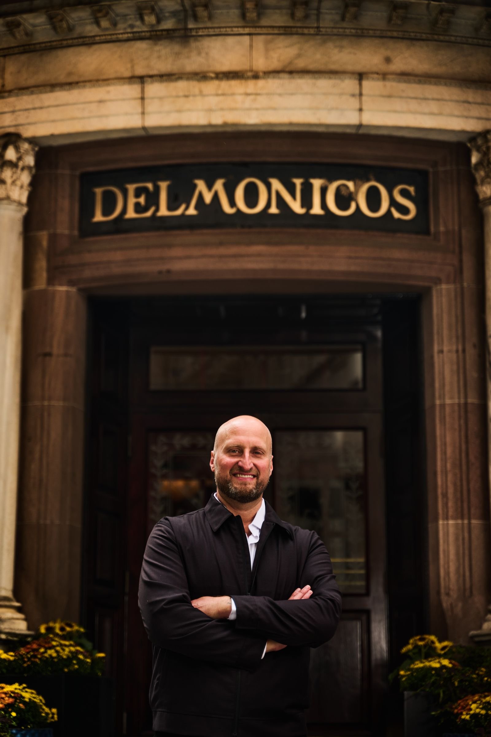 Dennis Turcinovic, arms crossed, under the carved Delmonico's entrance on Beaver Street