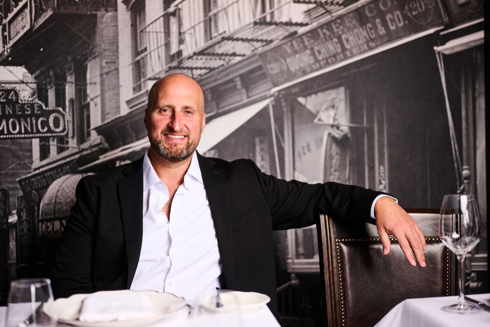 Dennis Turcinovic at a table in front of a mural of the nineteenth-century Delmonico's building