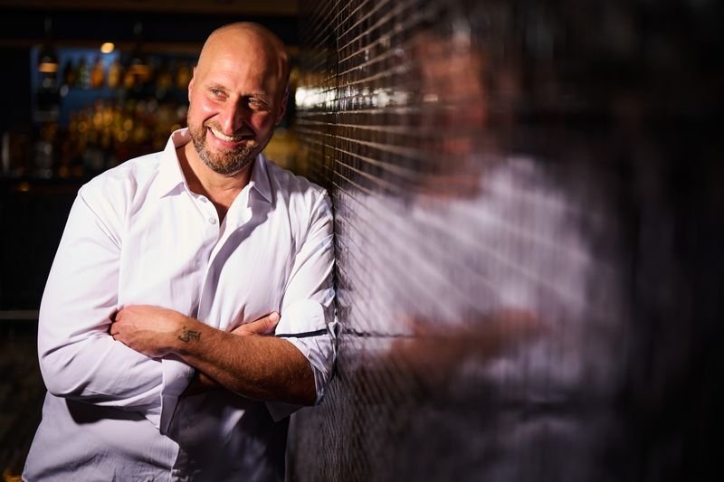 Dennis Turcinovic laughing, arms crossed, against a mosaic wall