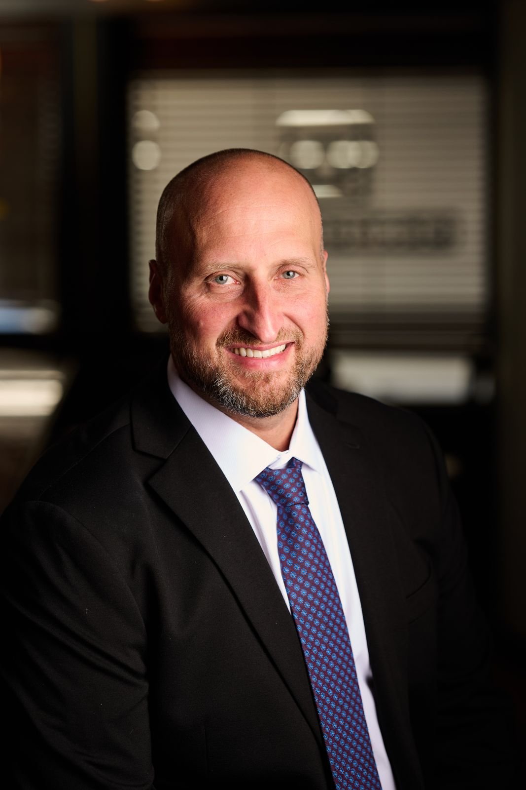 Portrait of Dennis Turcinovic in a dark suit and blue patterned tie, smiling, at Delmonico's