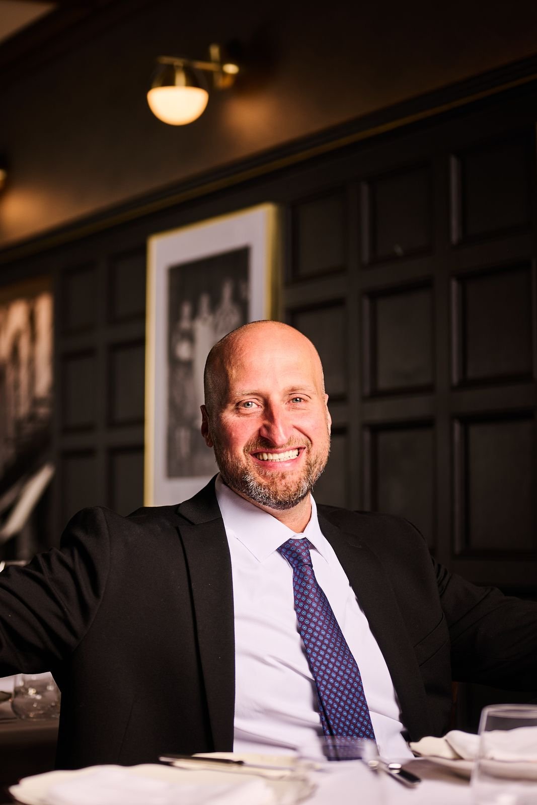 Dennis Turcinovic in a suit and tie, smiling at the head of a table in a Delmonico's private dining room