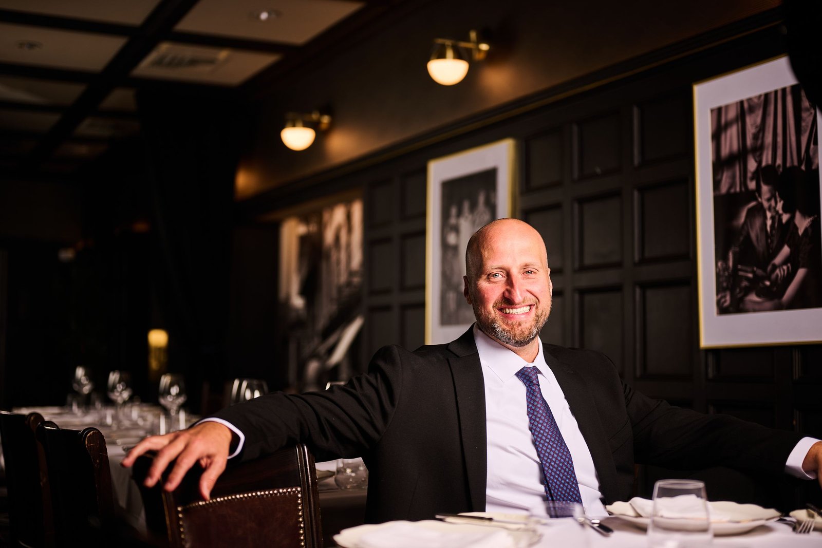 Dennis Turcinovic in a suit and tie, smiling at the head of a table in a Delmonico's private dining room